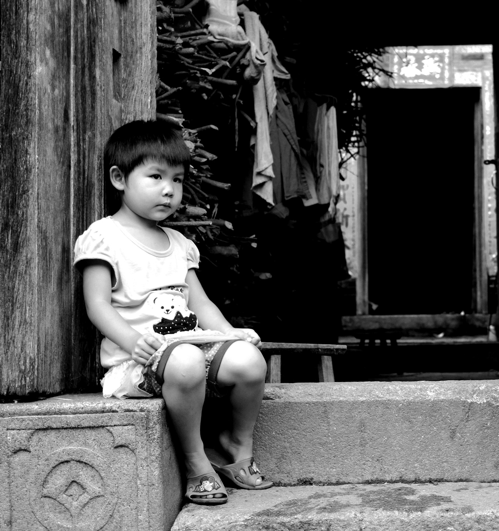 坐在门口的小女孩，也许她在想：爸爸妈妈你们什么时候回来？